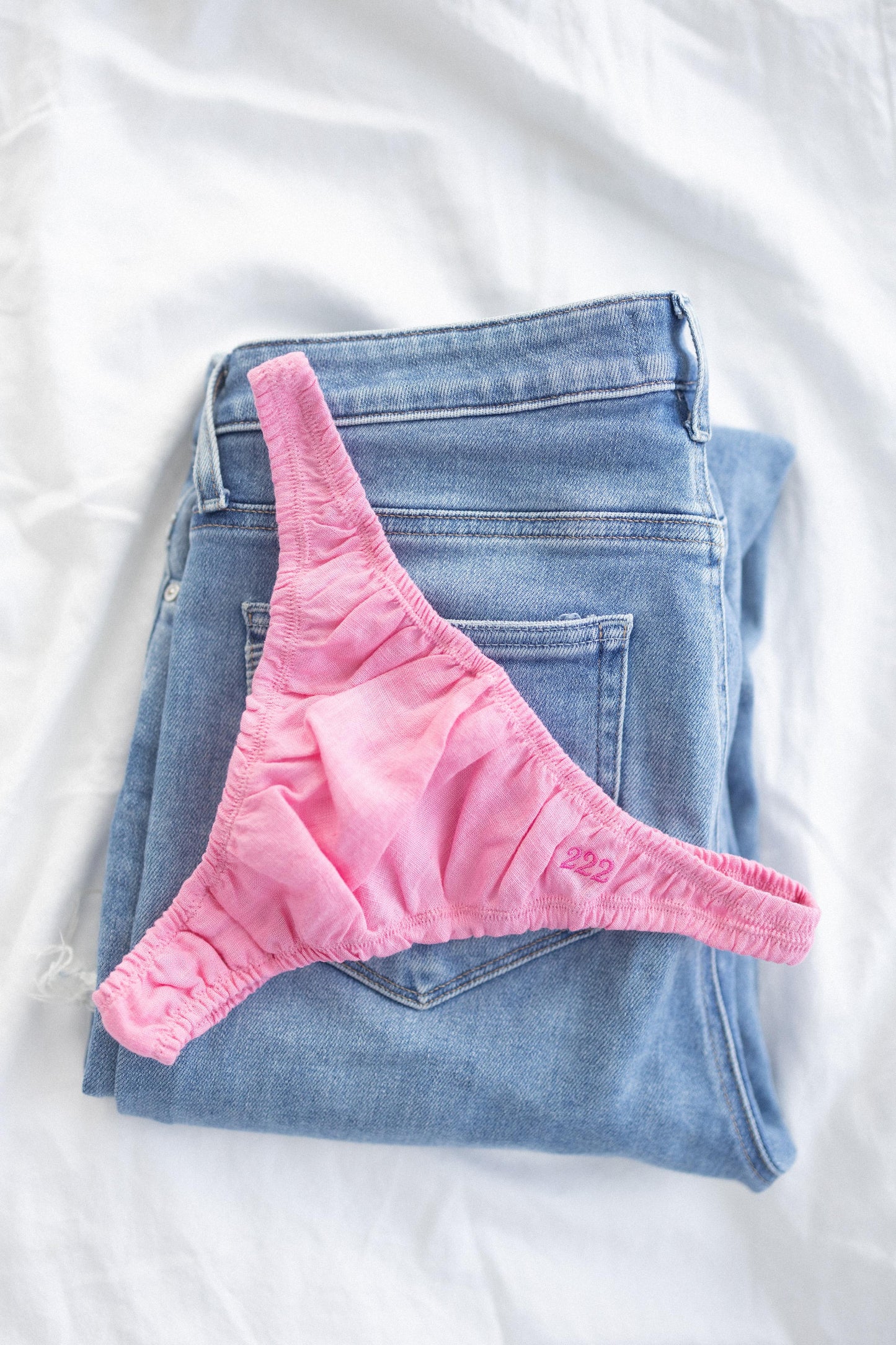 Pink linen thongs on folded blue jeans on a white background
